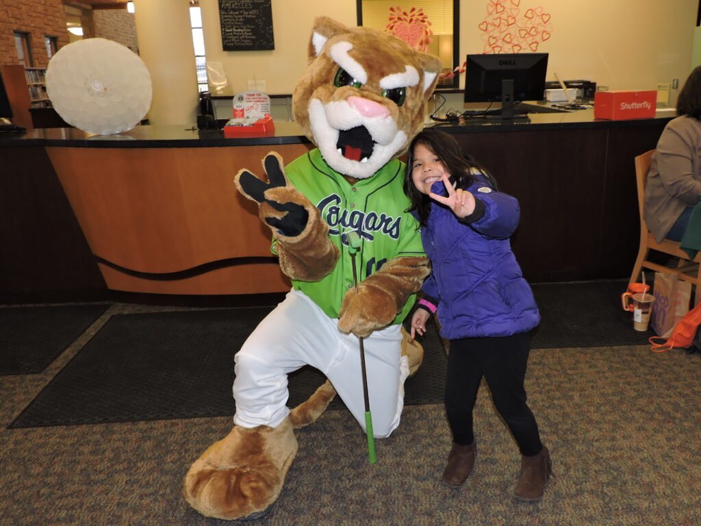 Cougar mascot shows peace sign with young girl also showing peace sign.