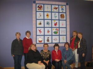 Eight women pose with new quilt on the wall