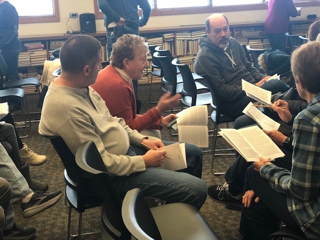 Five people sit in a semi circle with booklets describing suspects in murder mystery game